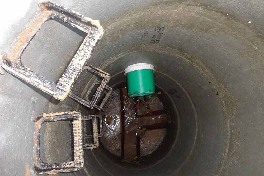 Aus einem Schachtdeckel kommt ein grünes Rohr.