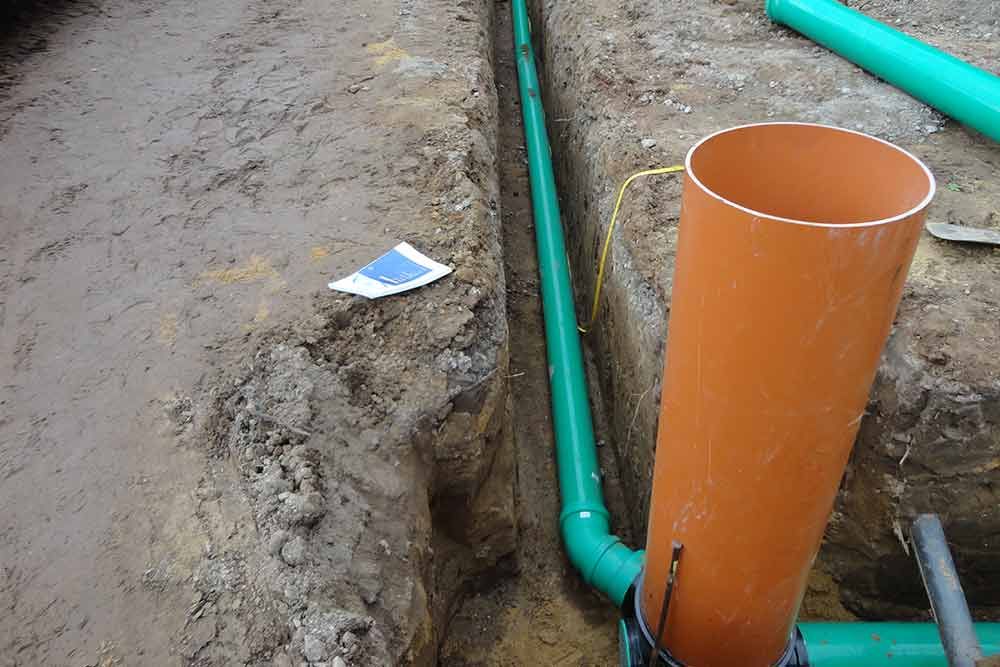 Ein orangefarbenes Rohr liegt im Dreck neben einem grünen Rohr.