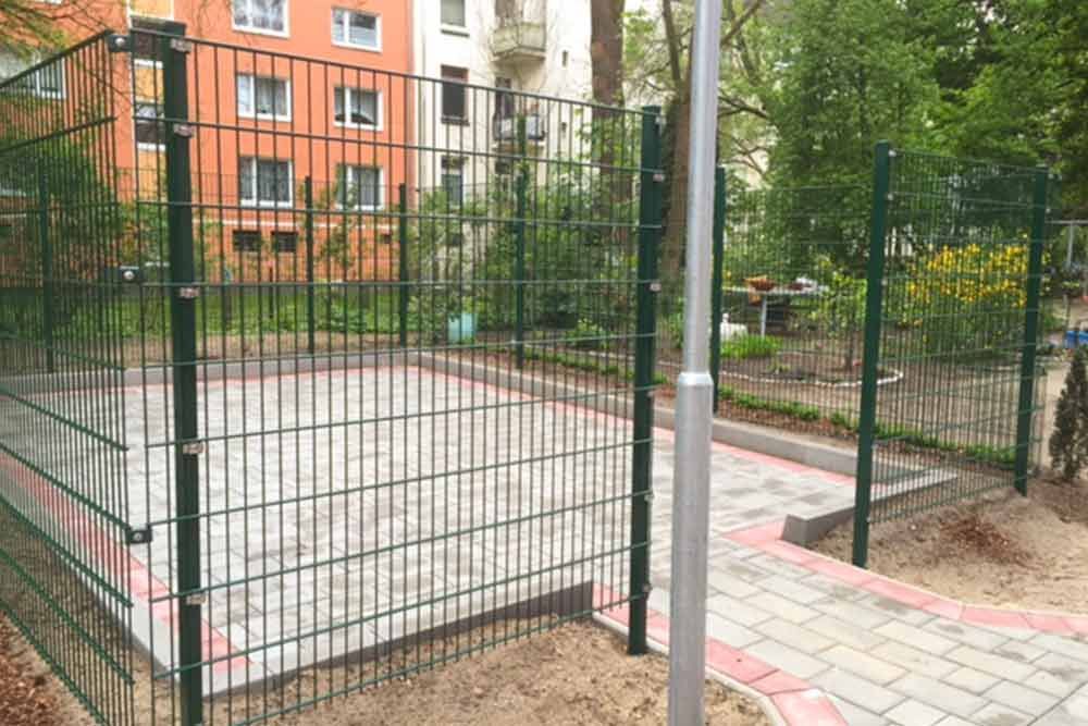 Ein Zaun umgibt einen Basketballplatz in einem Park.