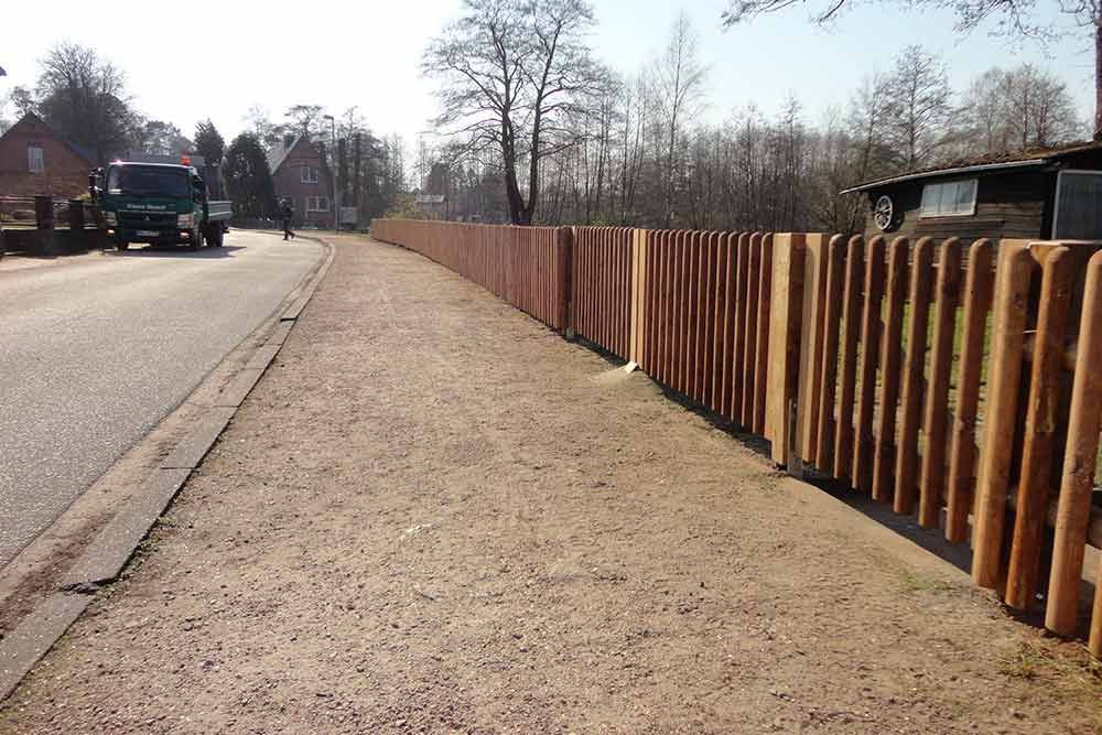 Ein Lastwagen fährt neben einem Holzzaun eine Straße entlang