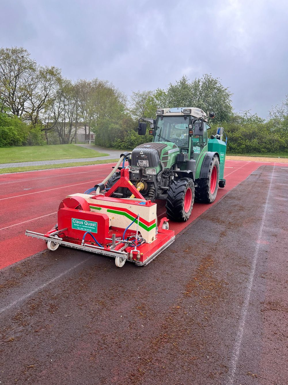 Ein grüner Traktor mit einer daran befestigten Maschine fährt einen Weg entlang.