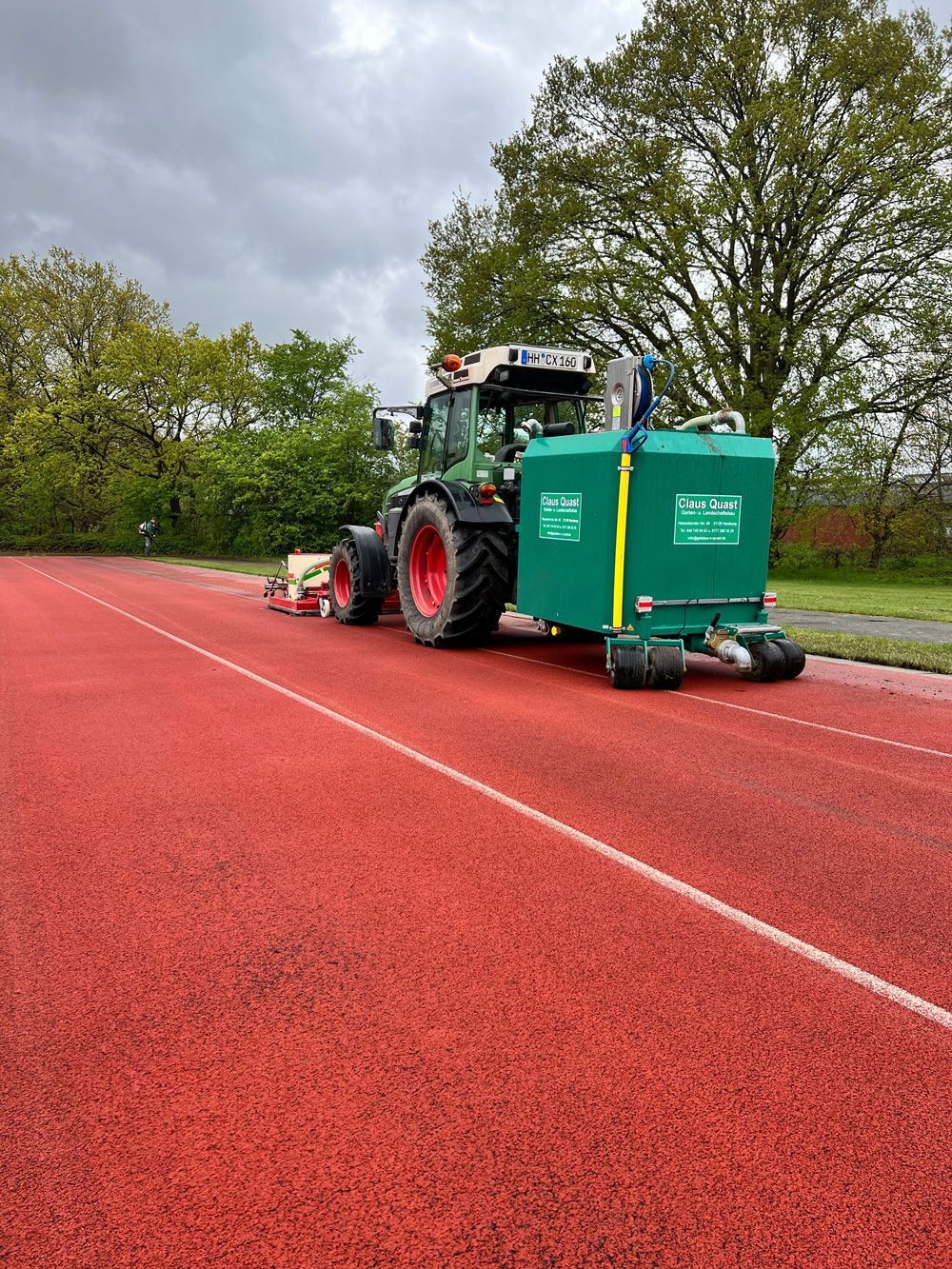 Ein grüner Traktor fährt einen roten Weg entlang.