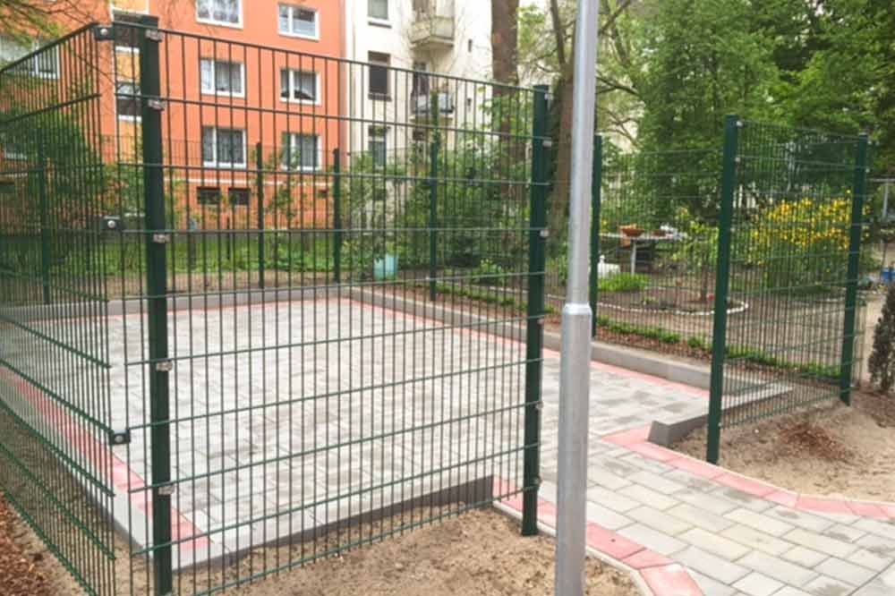 Ein grüner Zaun umgibt einen Basketballplatz in einem Park