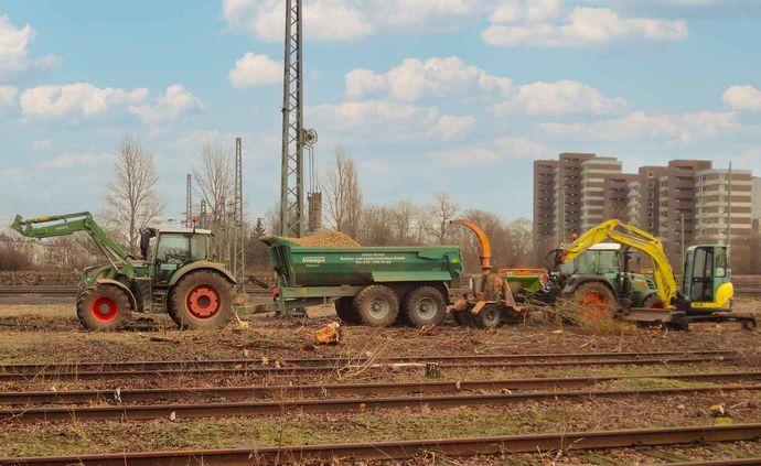 Ein Muldenkipper wird von zwei Traktoren auf einem Feld gezogen.