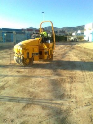 Un hombre conduce un rodillo amarillo en un camino de tierra.