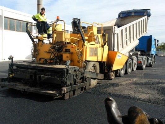 Un hombre está sentado encima de una máquina pavimentadora de asfalto amarilla.