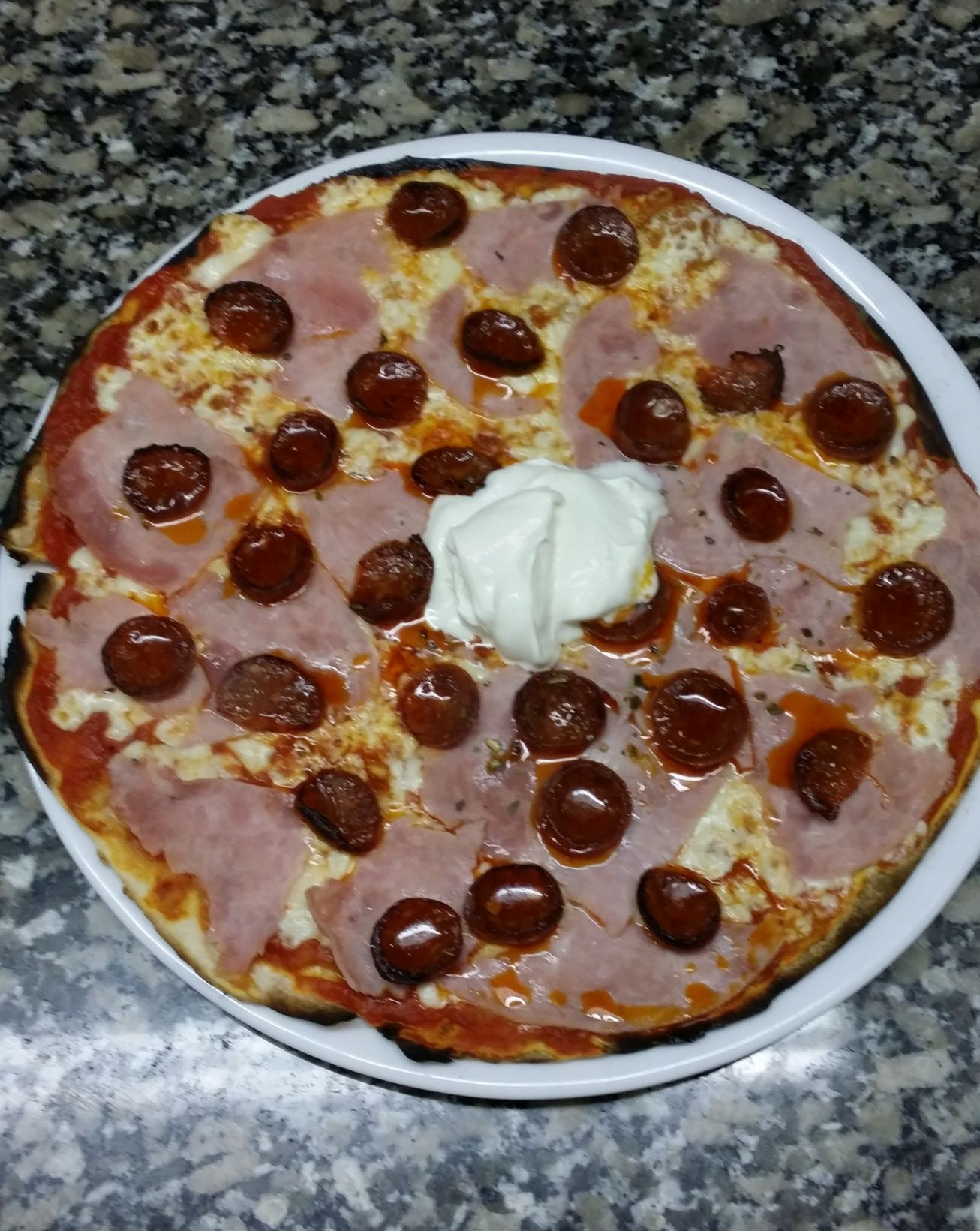 Pizza au jambon, au pepperoni et garnie d'une quenelle de crème fraîche sur une assiette blanche.