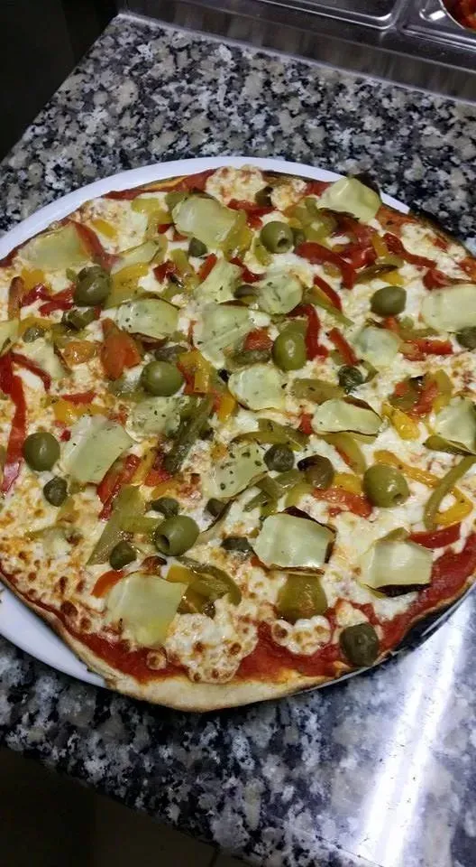 Pizza garnie de cœurs d'artichauts, d'olives vertes et de poivrons, servie sur une assiette blanche.