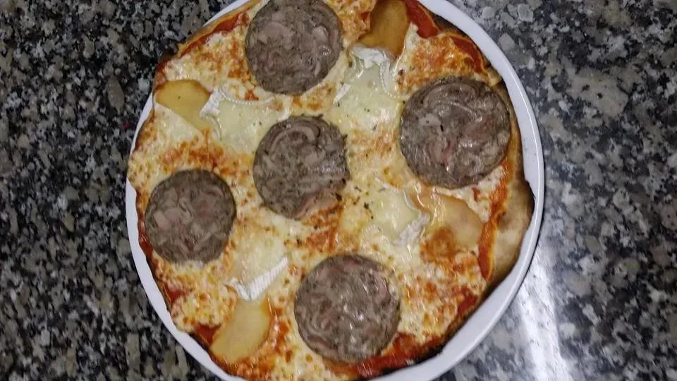 Pizza garnie de saucisse, de fromage blanc et de pommes de terre, servie dans un plat blanc.