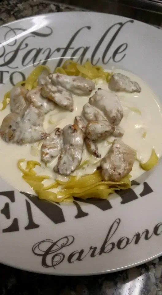 Plat de pâtes : Sauce crémeuse et morceaux de poulet sur des pâtes jaunes servies dans un bol décoratif.