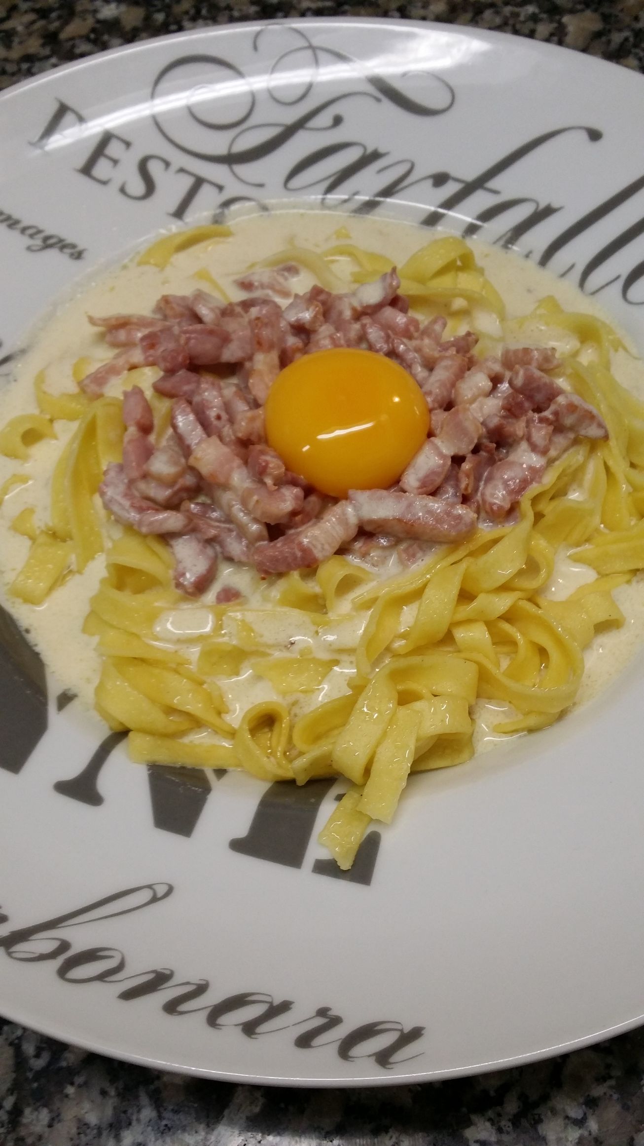 Fettuccine carbonara garnies de lardons et d'un jaune d'œuf cru, présentées dans une assiette décorative.