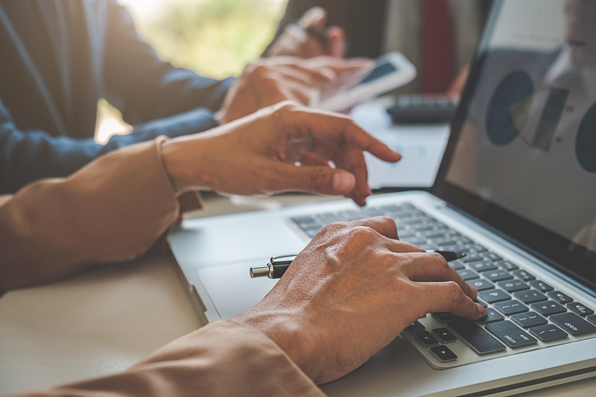 Ein Finanzwirt tippt auf einem Laptop, während eine andere Person auf ein Mobiltelefon schaut.