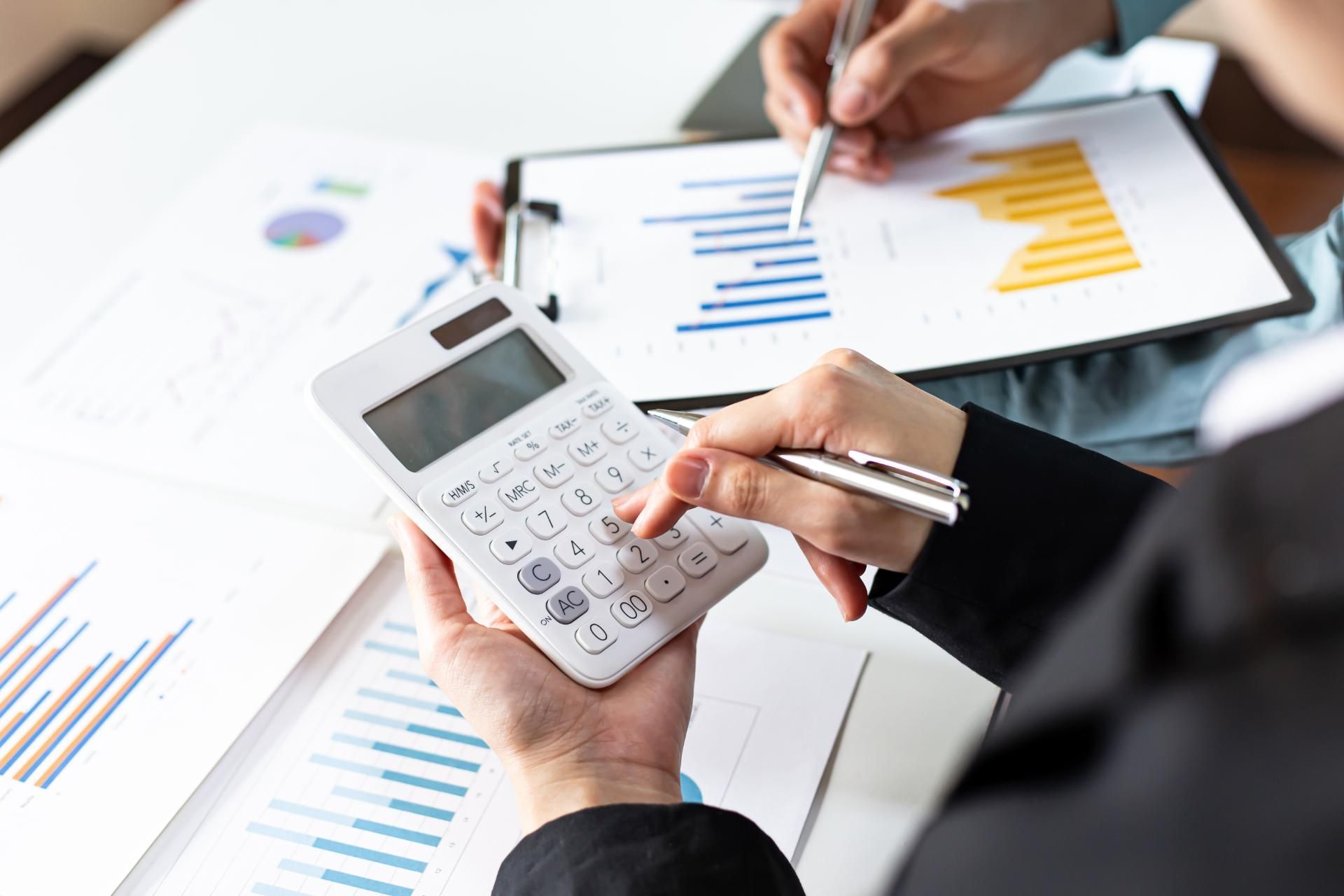 Ein Finanzwirt verwendet einen Taschenrechner, während eine andere Person auf einem Klemmbrett schreibt.