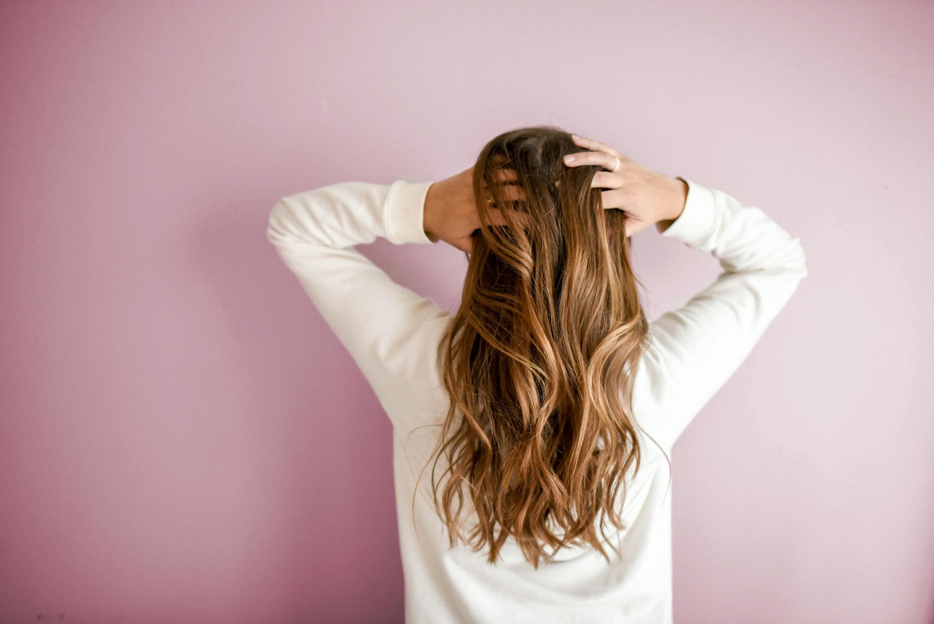 Una donna si tiene i capelli davanti a un muro rosa.