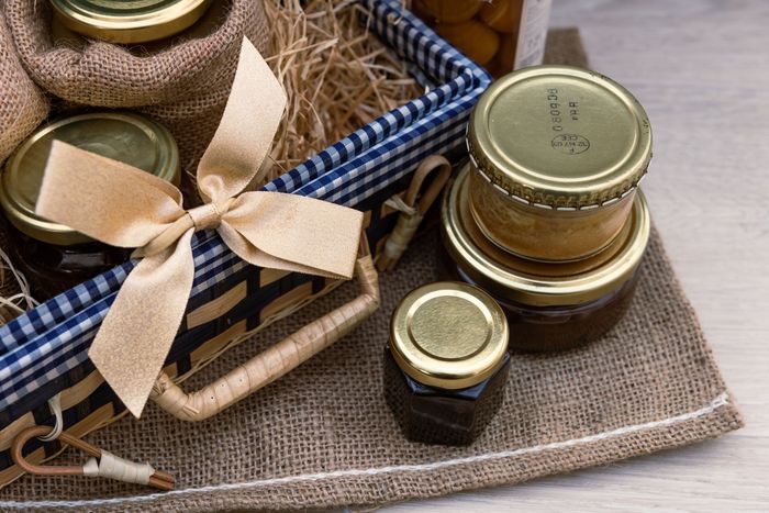 Petits bocaux en verre avec couvercles dorés et ruban beige, nichés dans un panier doublé de toile de jute à bordure vichy bleue et blanche.