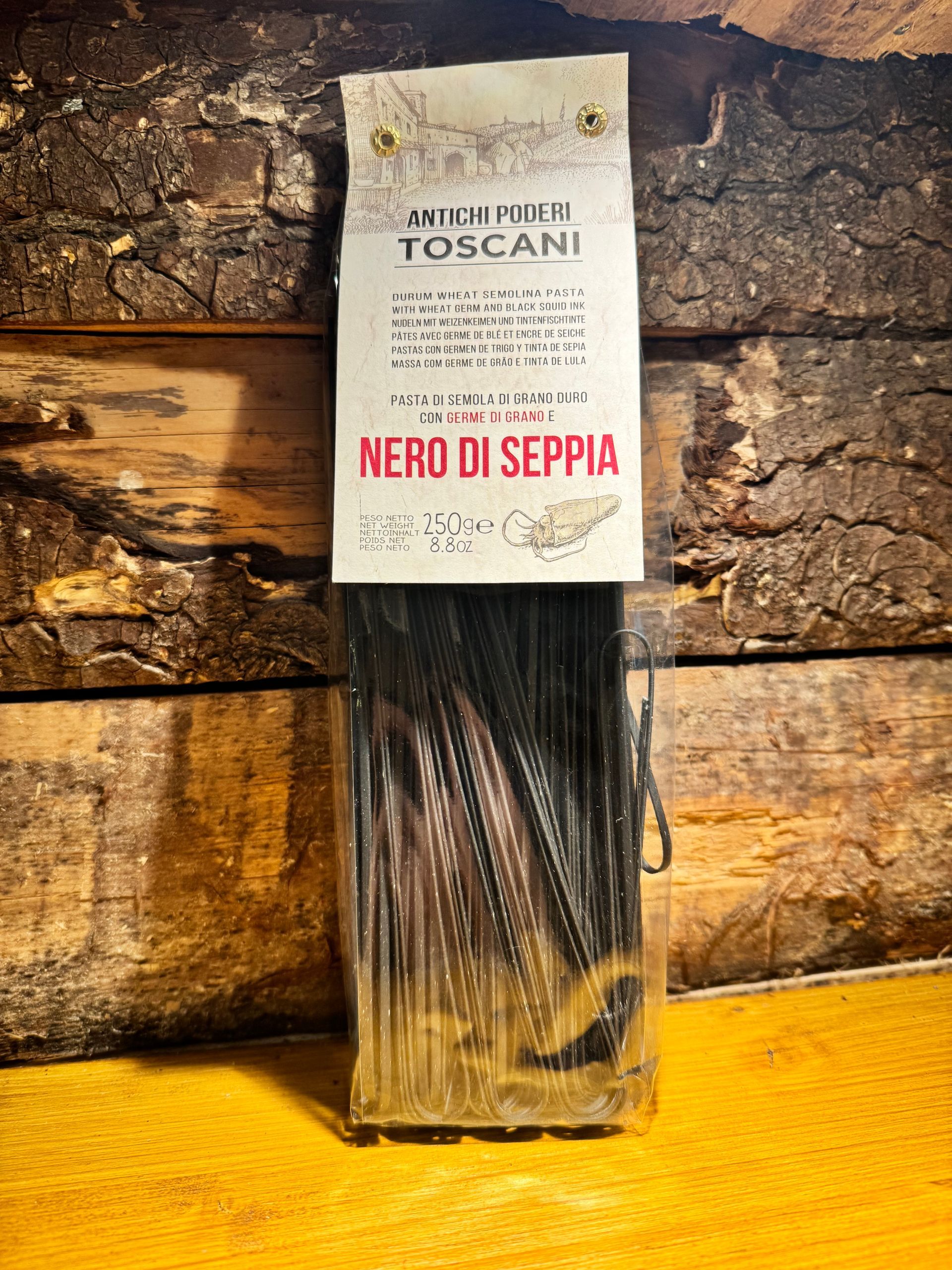 Un paquet de pâtes à l'encre de seiche noire, étiqueté « Nero di Seppia » posé sur une surface en bois, sur un fond de bois rustique.