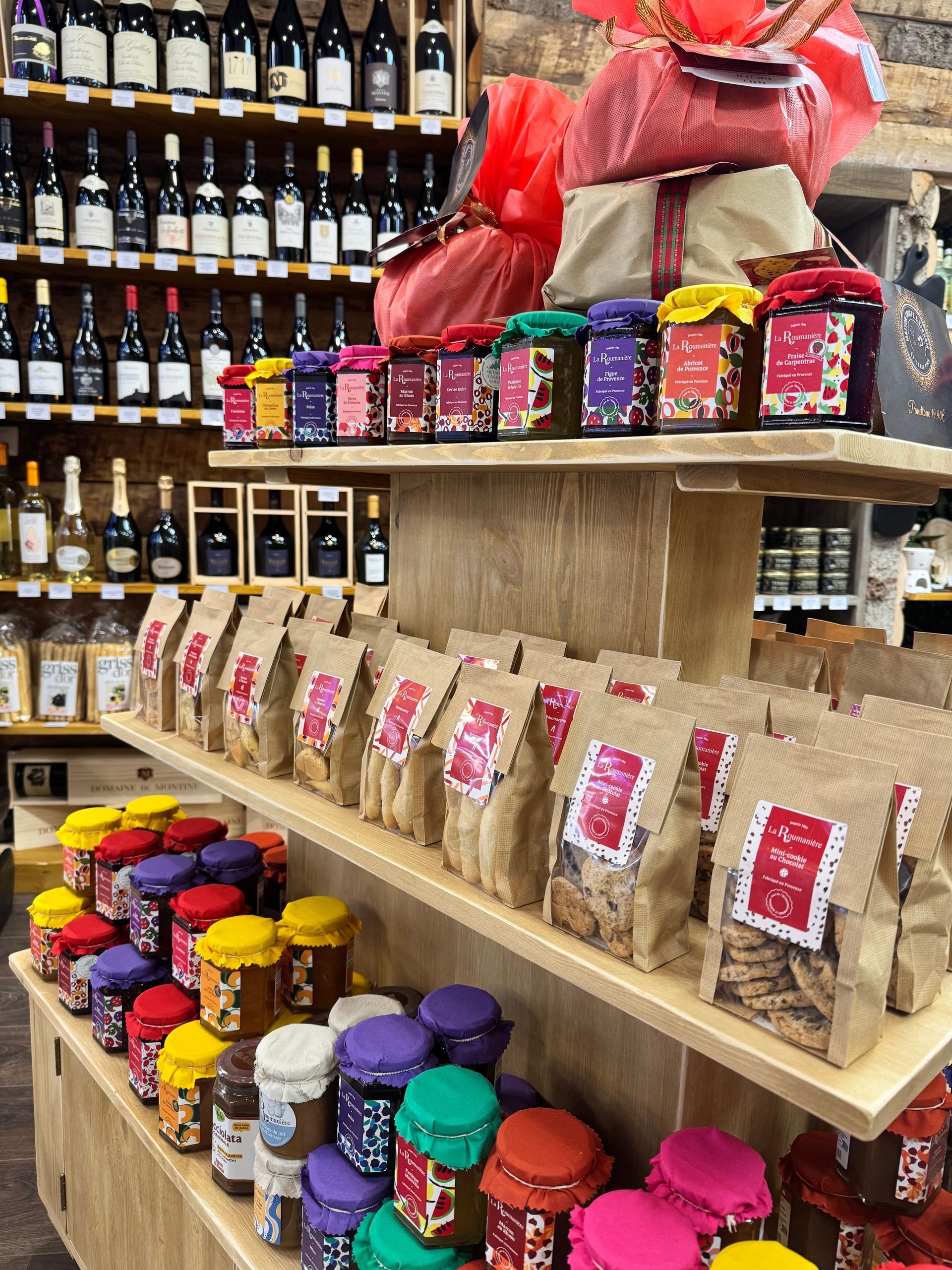 Des étagères dans un magasin présentent des bouteilles de vin, des bocaux assortis avec des couvercles colorés et des sacs de produits alimentaires.