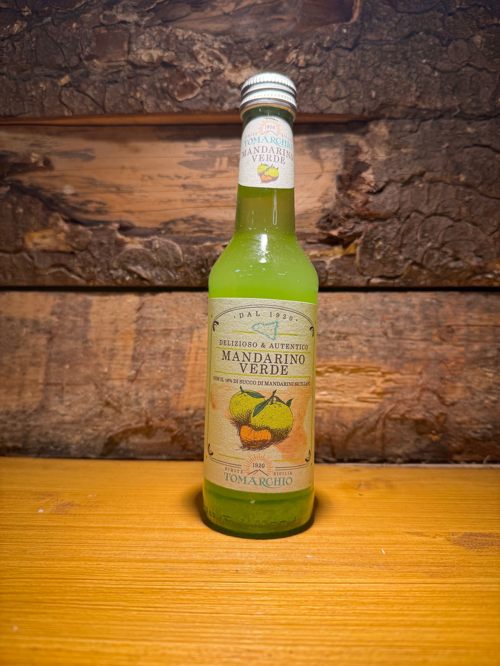 Une bouteille en verre vert de Limoncello Verde est posée sur une surface en bois clair, contre un mur rustique en planches de bois.