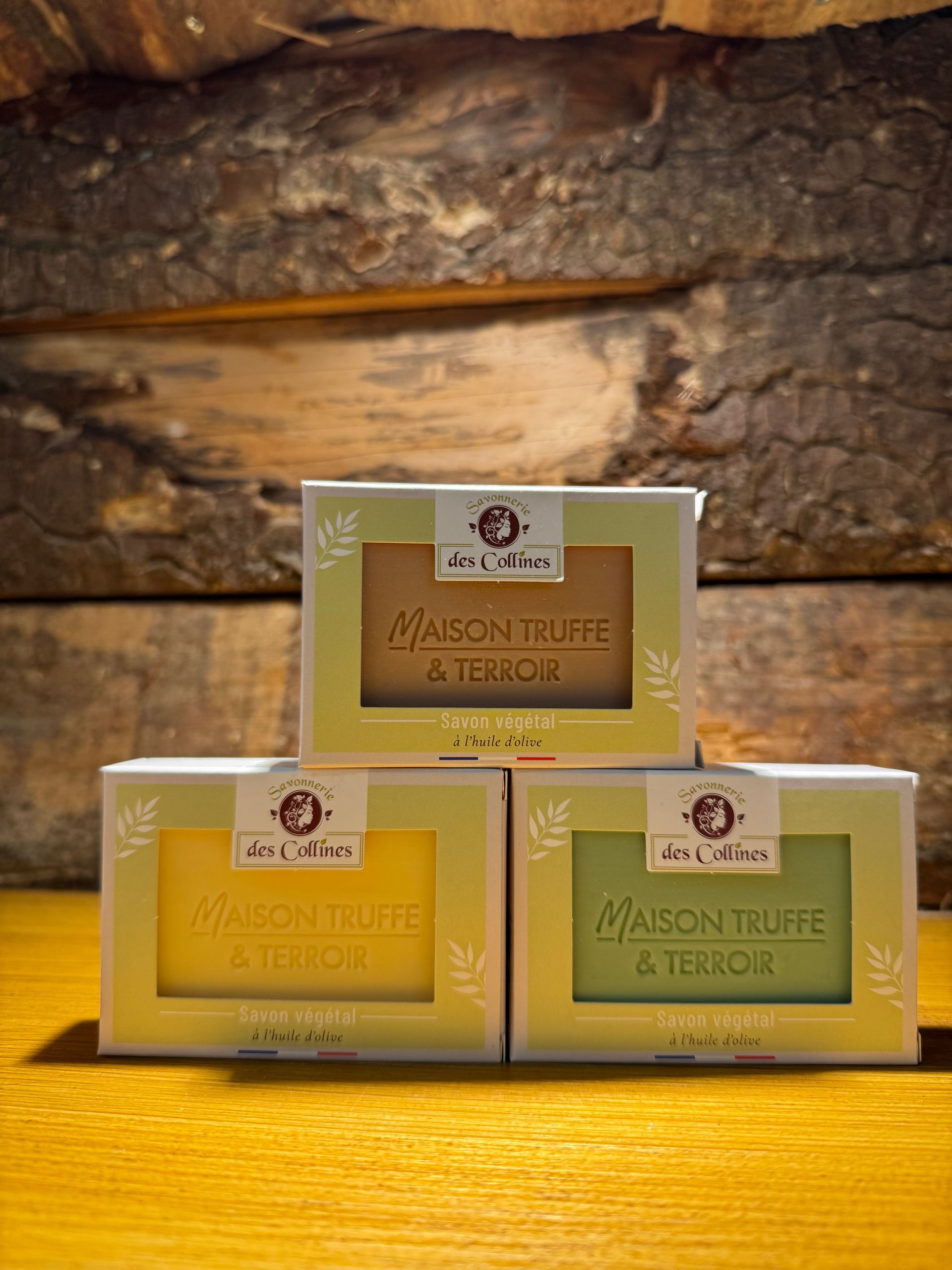 Trois pains de savon « Maison Truffe & Terroir », empilés en pyramide sur un fond de bois rustique.