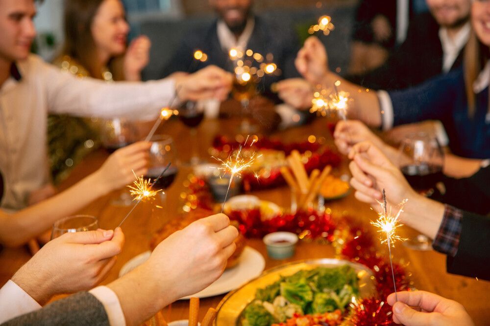 La gente brinda con bengalas alrededor de una mesa festiva llena de comida y bebidas