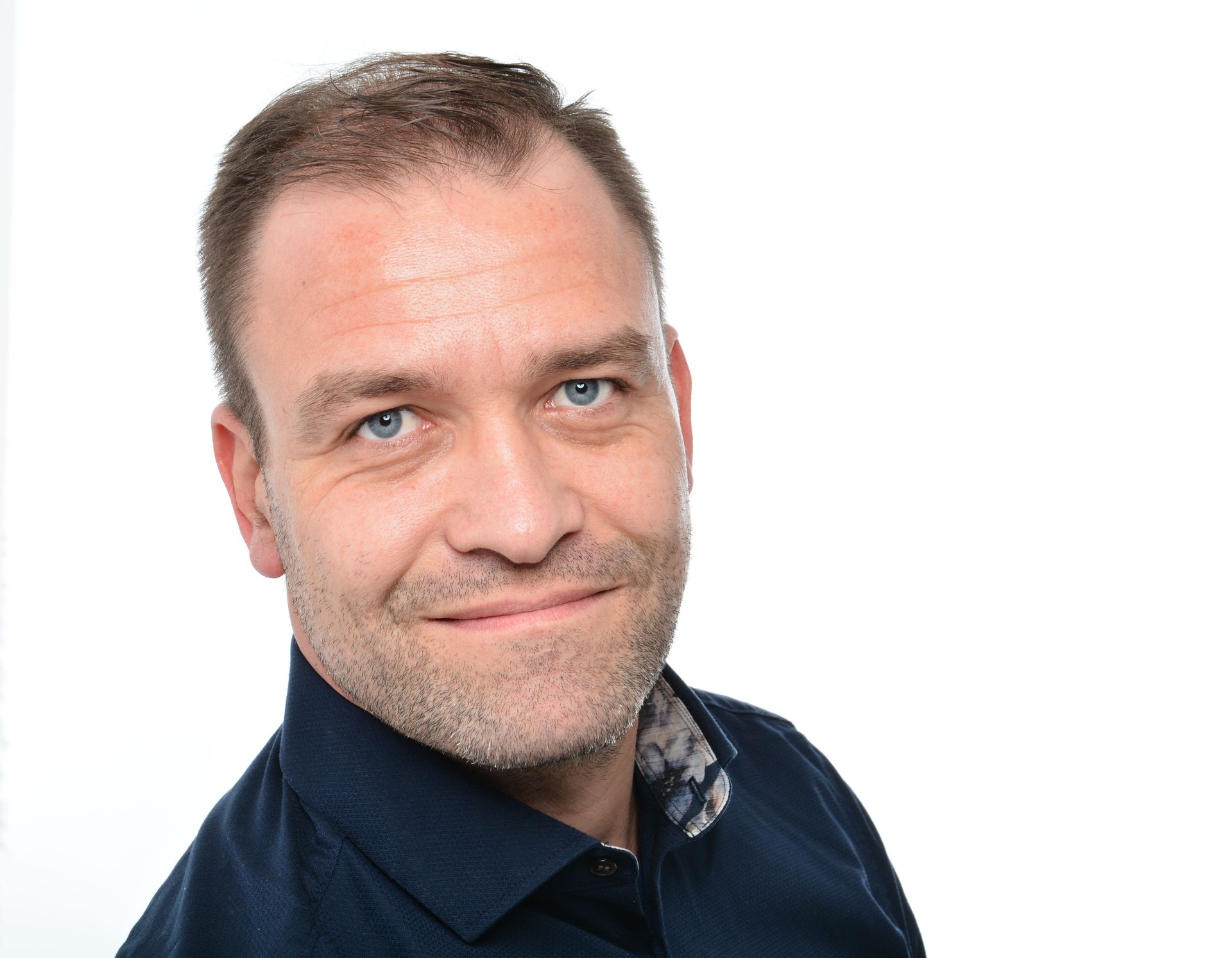 Porträt eines lächelnden Mannes in einem dunkelblauen Hemd vor weißem Hintergrund