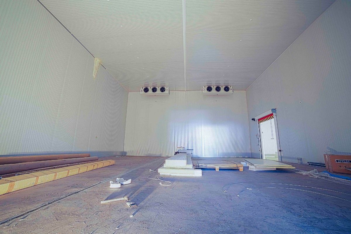 Interior de una cámara frigorífica industrial en construcción, con unidades de refrigeración montadas en la pared blanca aislada.