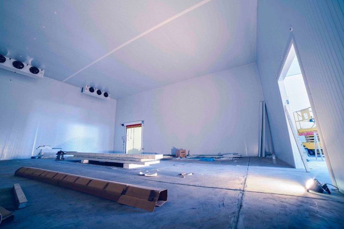 Cámara frigorífica industrial vacía, de paredes blancas, en construcción, con unidades de refrigeración instaladas en el techo.