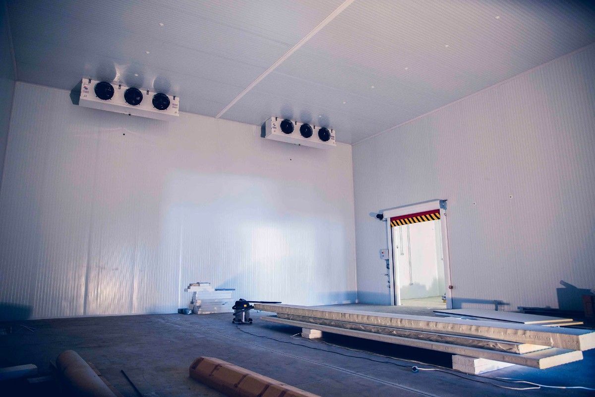 Una cámara frigorífica industrial vacía con dos unidades de refrigeración montadas en el techo y una puerta que da al exterior.