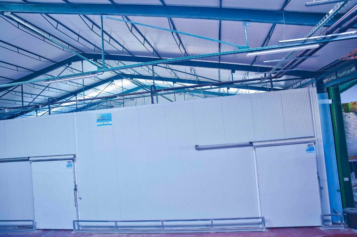 Un tabique industrial blanco con dos puertas correderas instalado bajo la estructura metálica del tejado de un almacén.