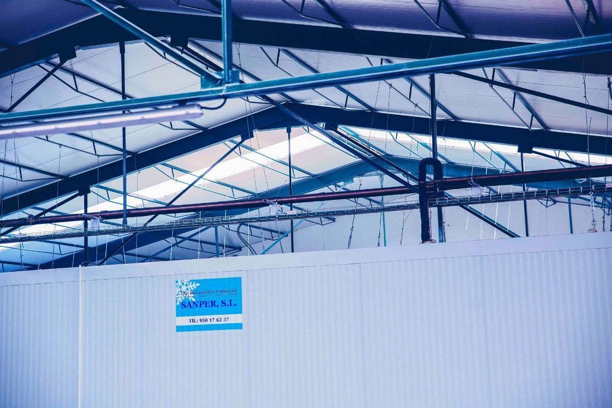 Un letrero azul y blanco fijado a una pared blanca en el interior de un edificio con un techo industrial alto y a la vista.