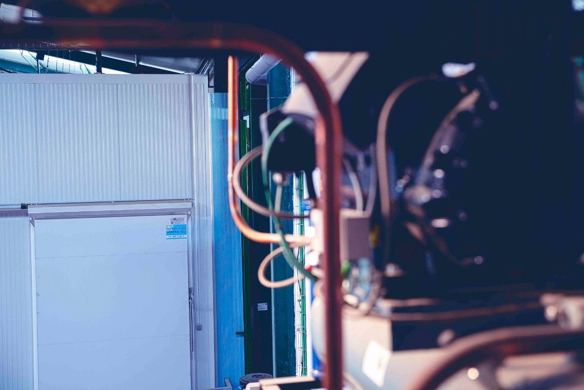 Vista de cerca de tuberías de cobre y cableado eléctrico con un fondo de equipos de refrigeración industrial.