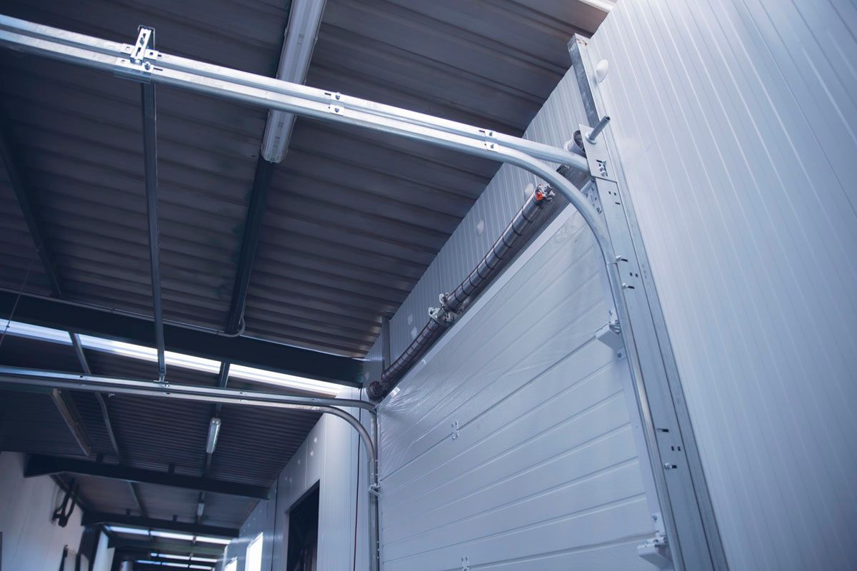 Vista desde un ángulo bajo de los rieles de una puerta de garaje industrial y los paneles blancos instalados contra la estructura del techo.