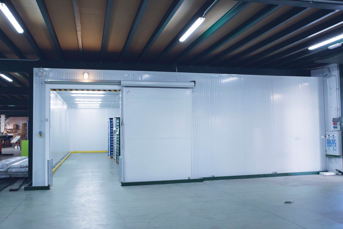Una puerta corredera blanca da acceso a un almacén aséptico y bien iluminado dentro de una nave industrial.
