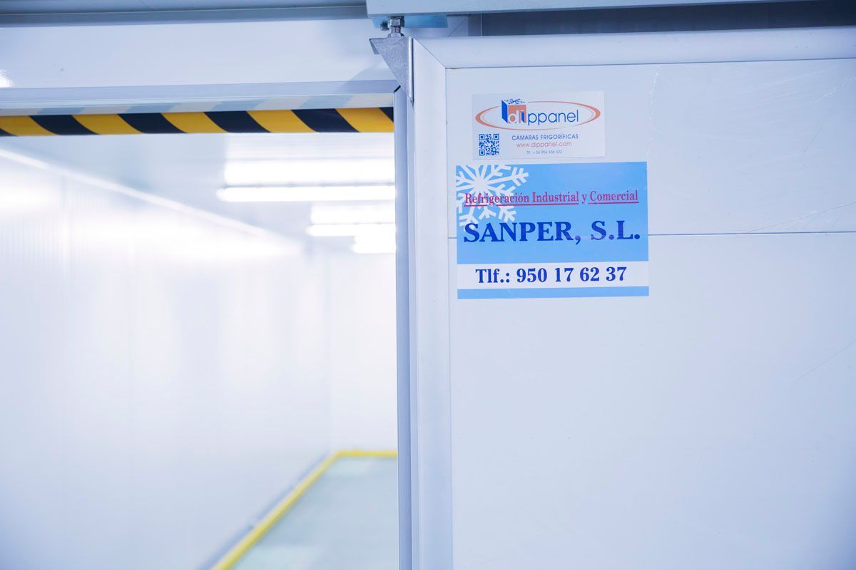 Una puerta abierta da a una cámara frigorífica industrial blanca y limpia con una etiqueta que dice 