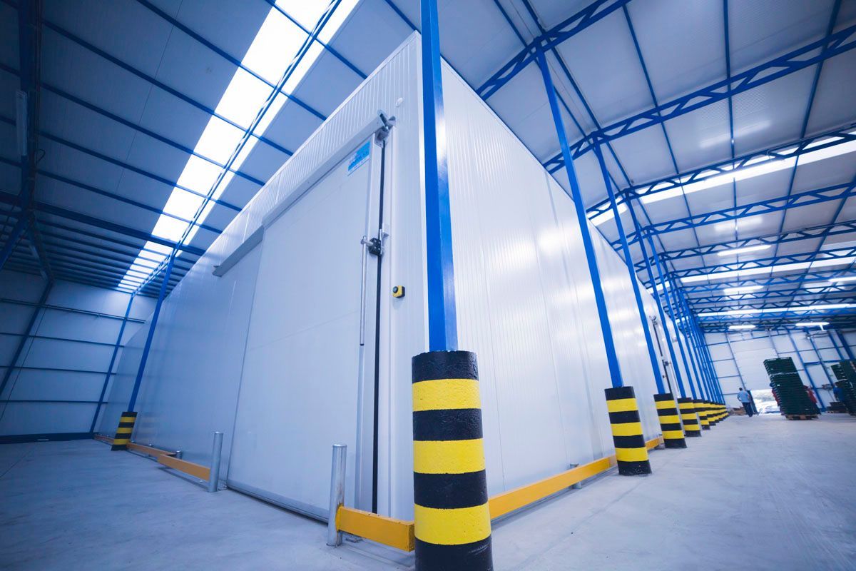 Grandes unidades industriales blancas de almacenamiento en frío en un almacén con vigas de soporte de acero azul y topes de seguridad amarillos.
