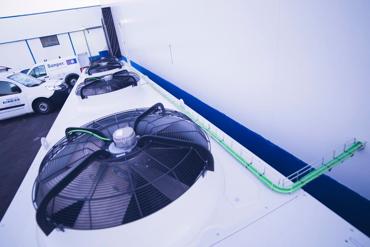 Grandes ventiladores industriales en una azotea blanca con conductos eléctricos verdes que recorren la pared.