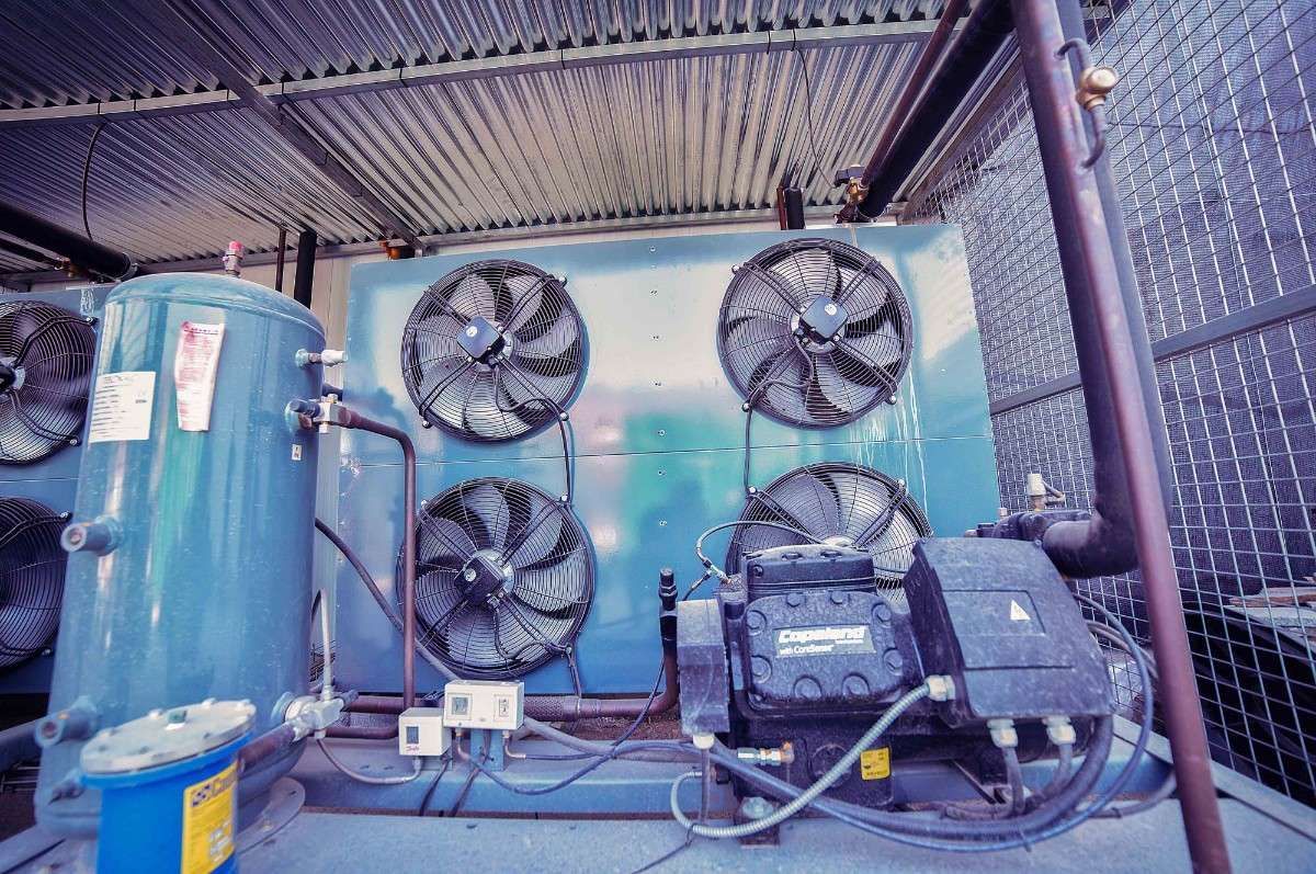 Unidad de refrigeración industrial con cuatro ventiladores circulares montados en un panel azul junto a un depósito metálico y un motor negro.