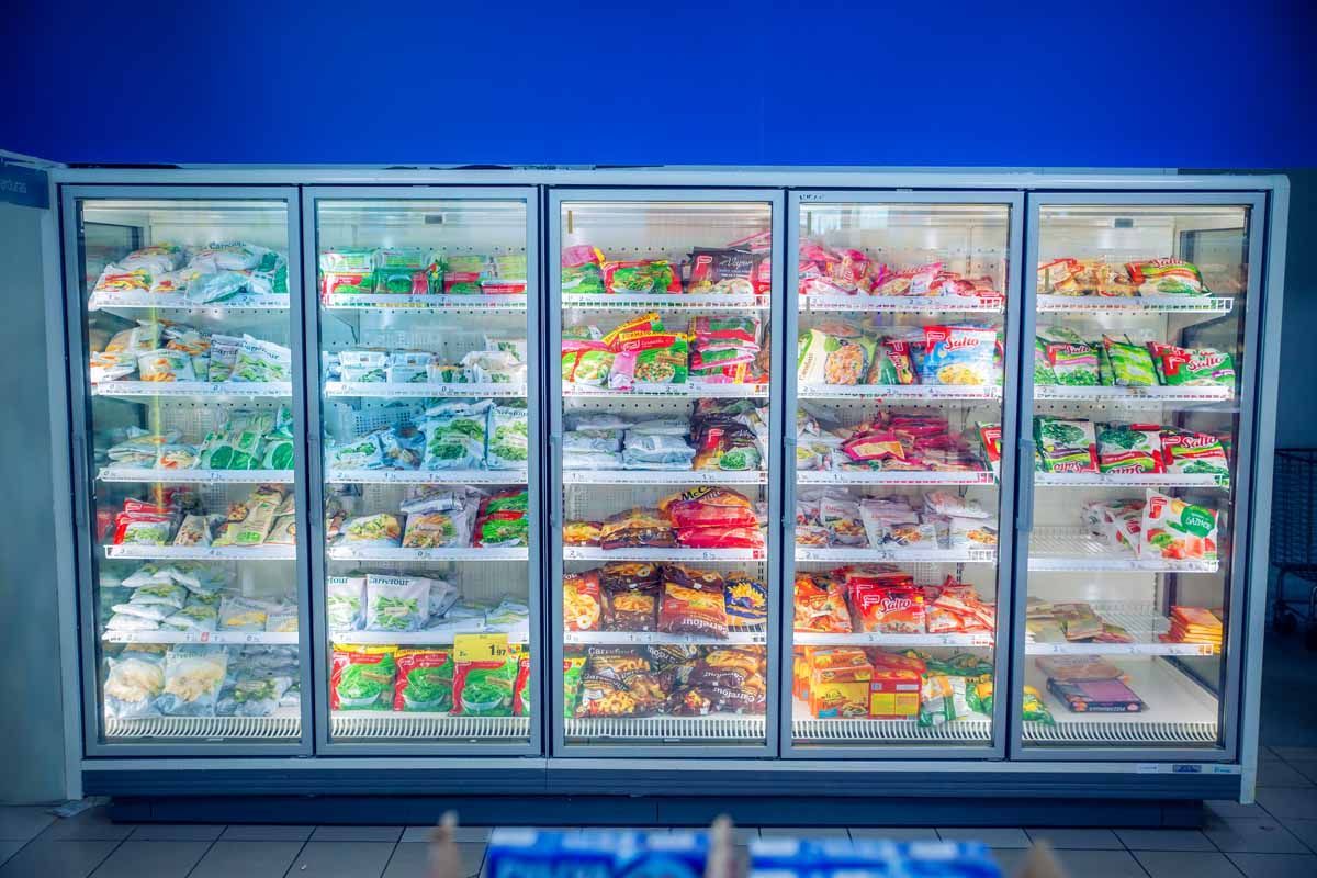 Una gran vitrina refrigerada comercial de cinco secciones, repleta de bolsas de alimentos congelados de diferentes tamaños, ubicada en una tienda.