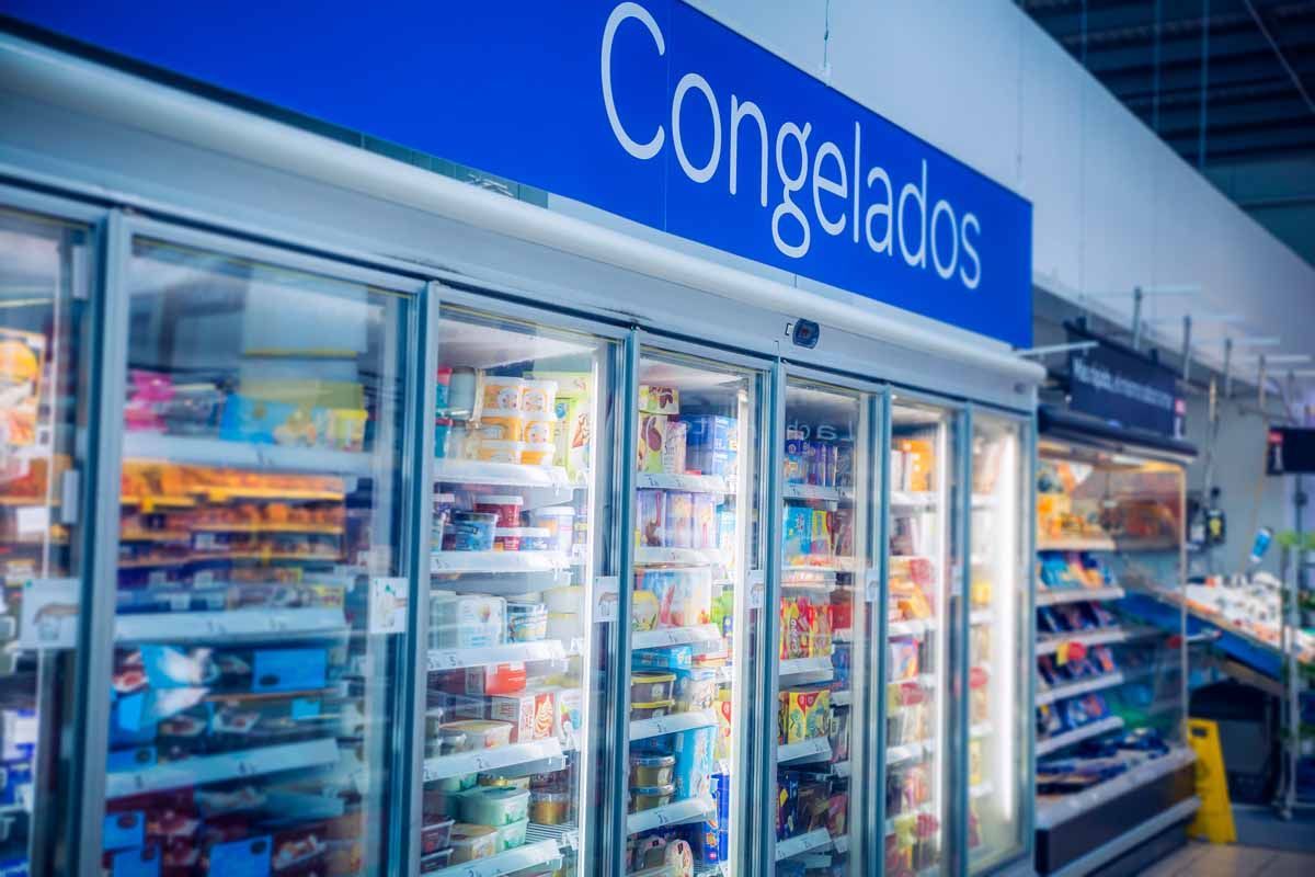 Una hilera de vitrinas congeladoras con frente de vidrio en un supermercado con un letrero azul encima que dice 