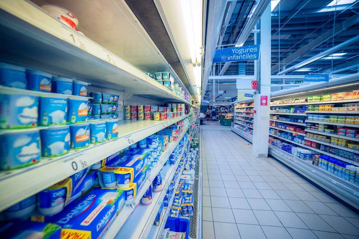 Vista en perspectiva de un pasillo de supermercado bien iluminado, con estantes repletos de diversos productos lácteos.