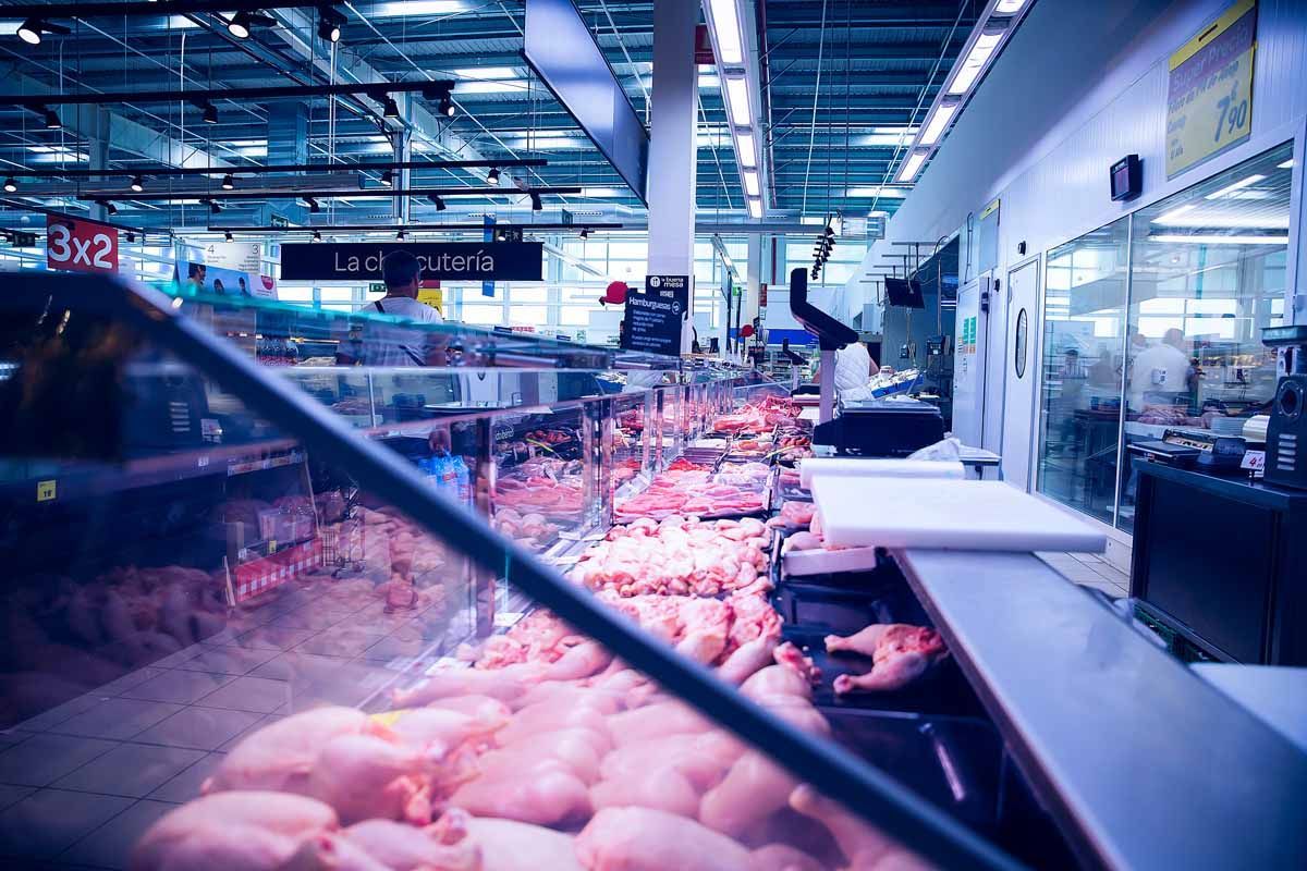 Un mostrador de carne de supermercado que exhibe varios cortes de pollo crudo bajo una brillante iluminación fluorescente.