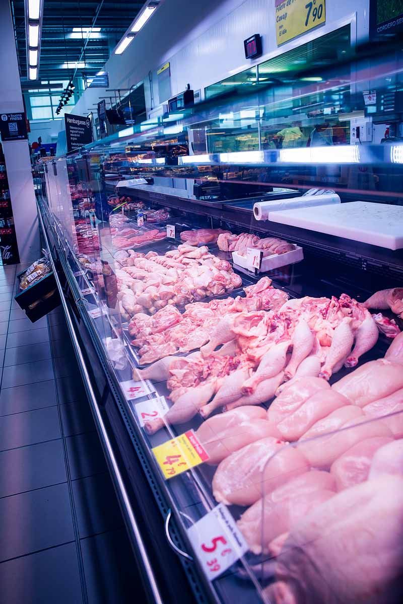 Una vitrina refrigerada en un supermercado llena de diferentes cortes de pollo crudo con las etiquetas de precio visibles.