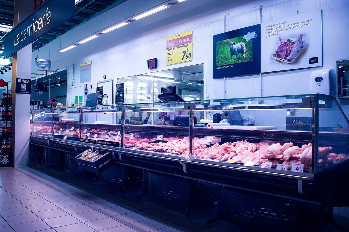 Una toma panorámica de un mostrador de carne de supermercado lleno de varios cortes de carne cruda bajo una iluminación brillante de tonos fríos.