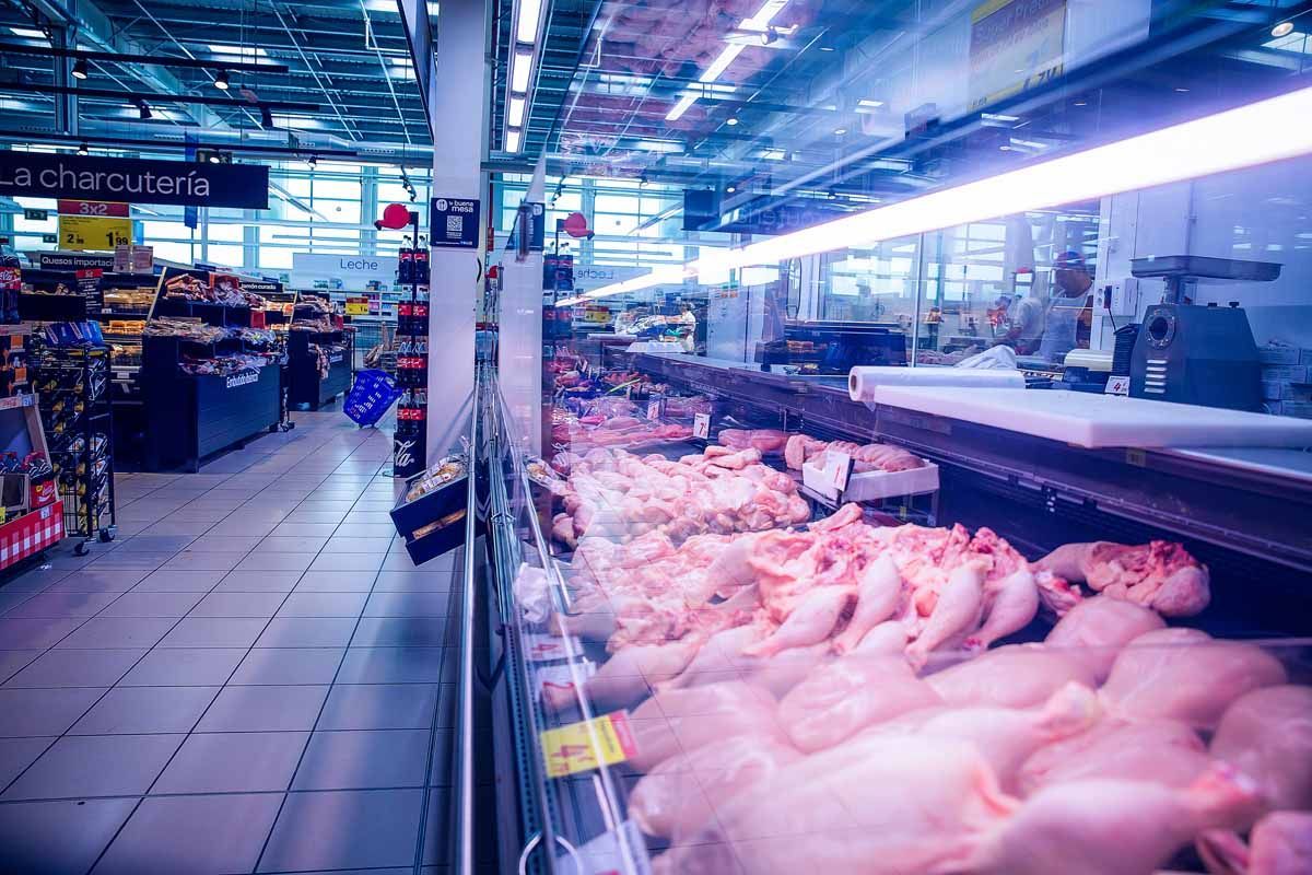Un mostrador de carne de supermercado que exhibe varios trozos de pollo crudo bajo luces brillantes.