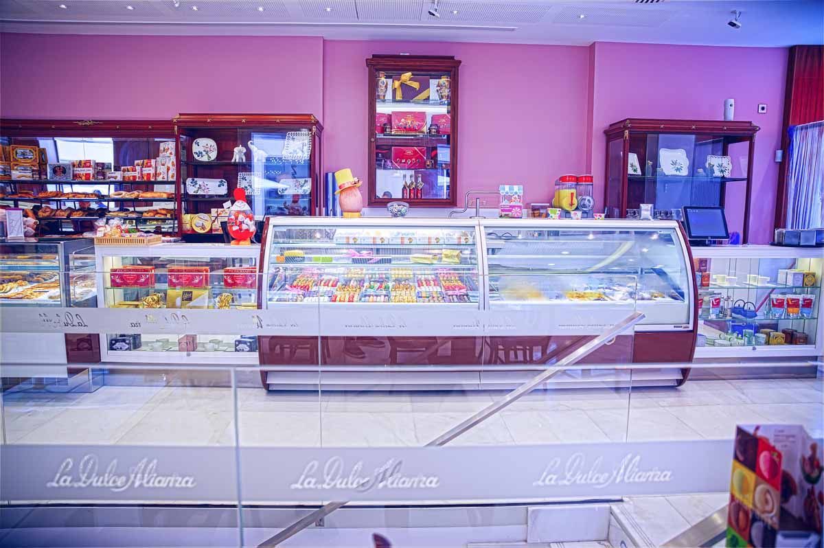 Un mostrador de panadería con vitrinas repletas de pasteles y bollería, contrastando con una pared de color rosa vibrante.