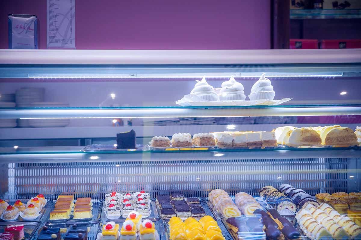 Una vitrina refrigerada en una panadería, repleta de pasteles, bollería y postres variados en múltiples estantes de cristal.