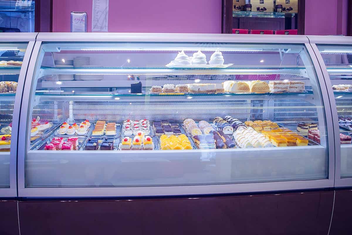 Una vitrina de cristal repleta de una variedad de pasteles y postres coloridos, en un ambiente de panadería.