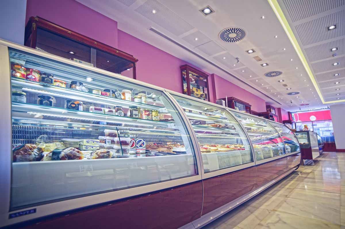 Una larga vitrina refrigerada repleta de pasteles y productos horneados en una tienda moderna de paredes moradas.