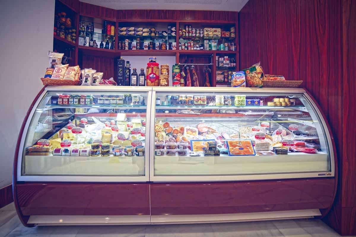 Una vitrina refrigerada repleta de productos gourmet, con estantes detrás que ofrecen diversos productos de alimentación.
