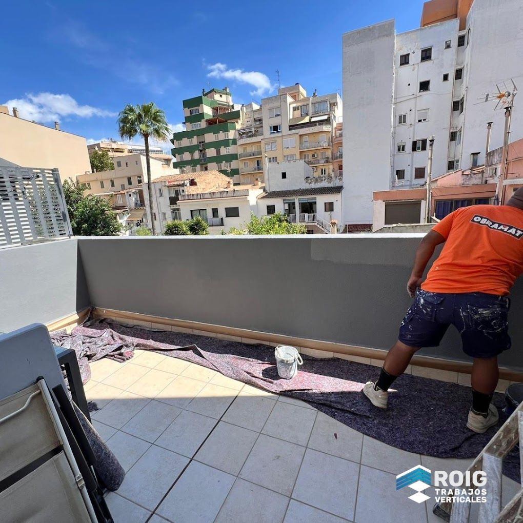 Un hombre con una camisa naranja está pintando una pared en un balcón.